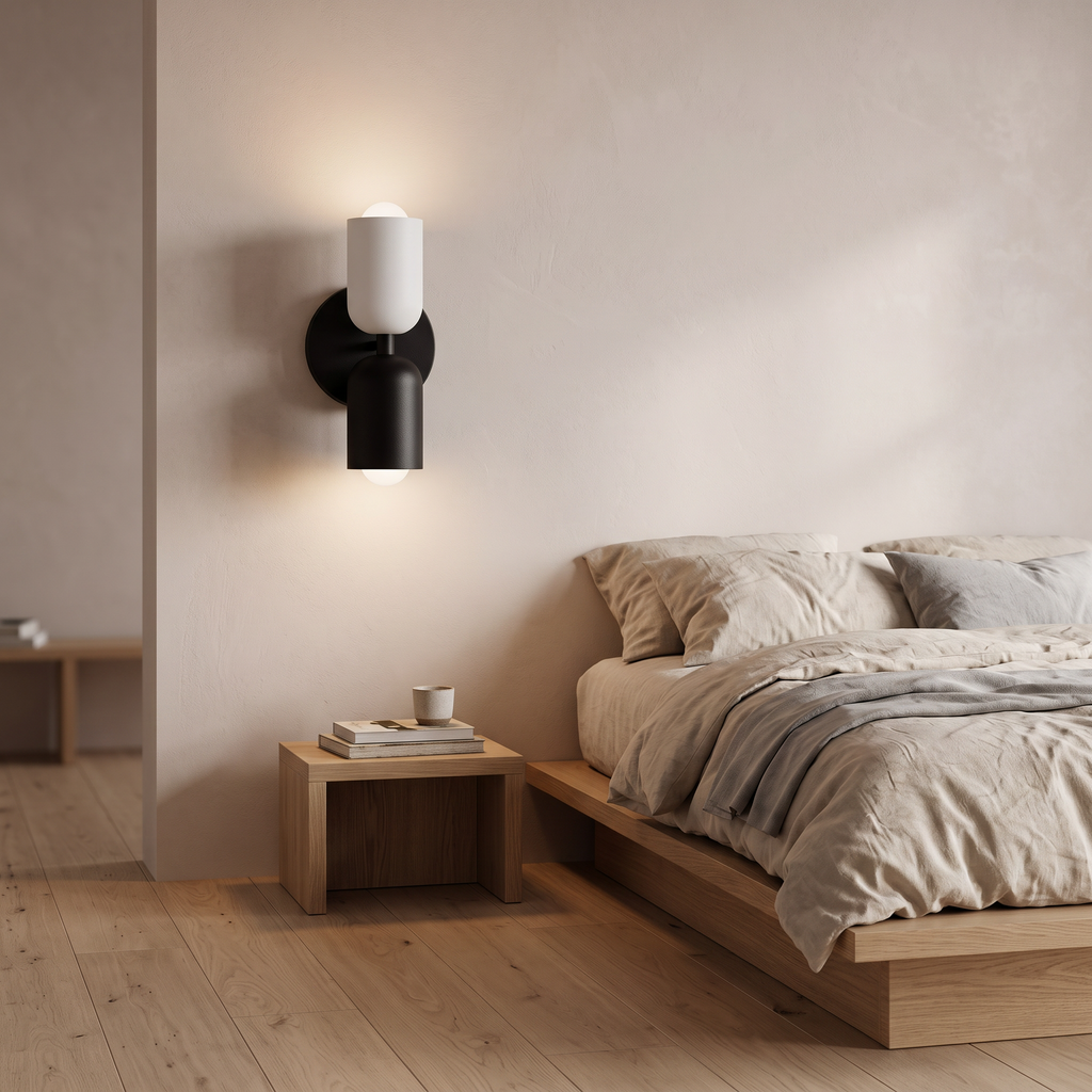 Bedside wall light with white upper shade and black lower shade, lit beside a bed